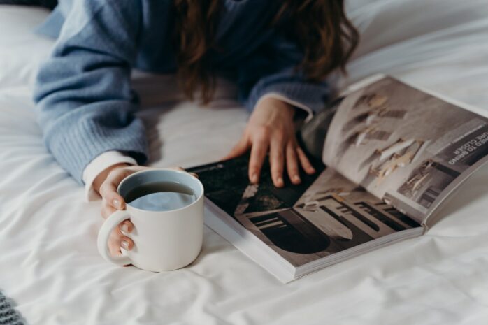 Woman lying on a bed and looking at an image in a book and a cup of coffee