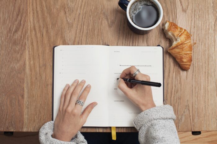 Hands writing on a notebook with a coffee and a croissant