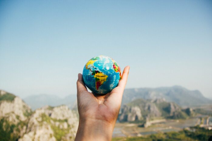 Hand holding a small globe in front of a landscape