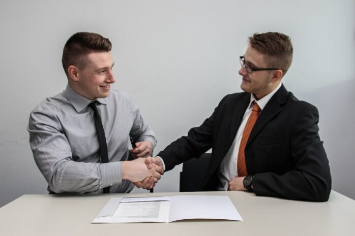 Two men wearing ties shaking hands on a desk